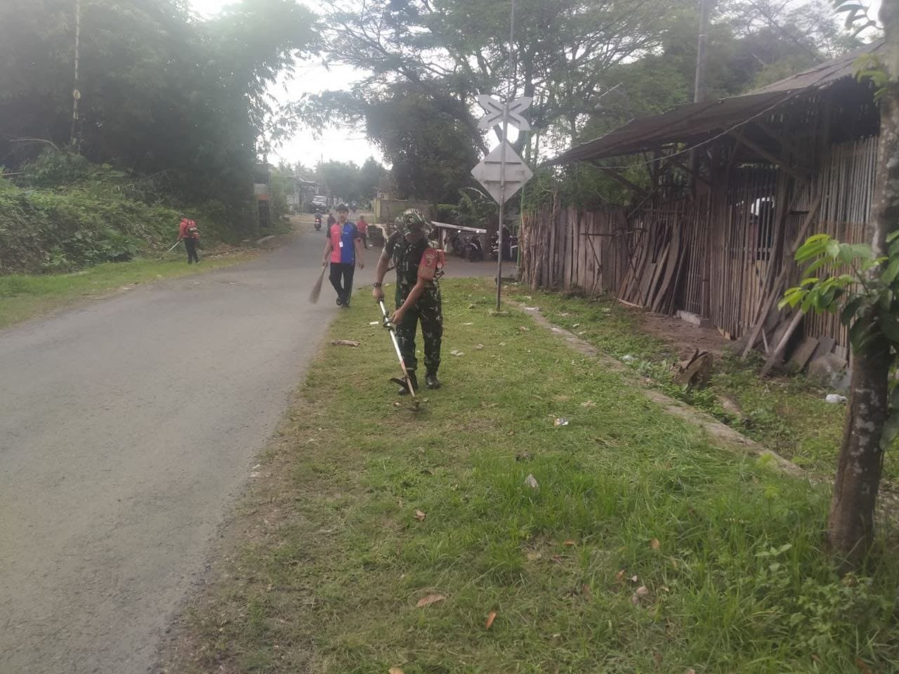 Babinsa Koramil Rogojampi Gandeng Warga Timurejo Bersihkan Rumput Liar di Bahu Jalan